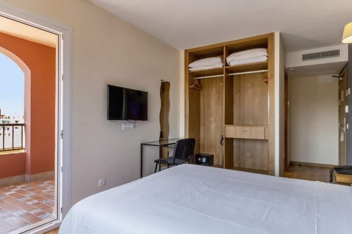 Une chambre d’hôtel comprenant un lit, un bureau, une télévision, une armoire et un balcon.