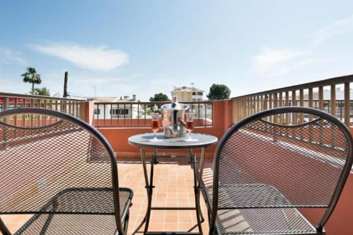 Une terrasse avec deux chaises en métal et une table, une bouteille de champagne et des verres posés sur la table.