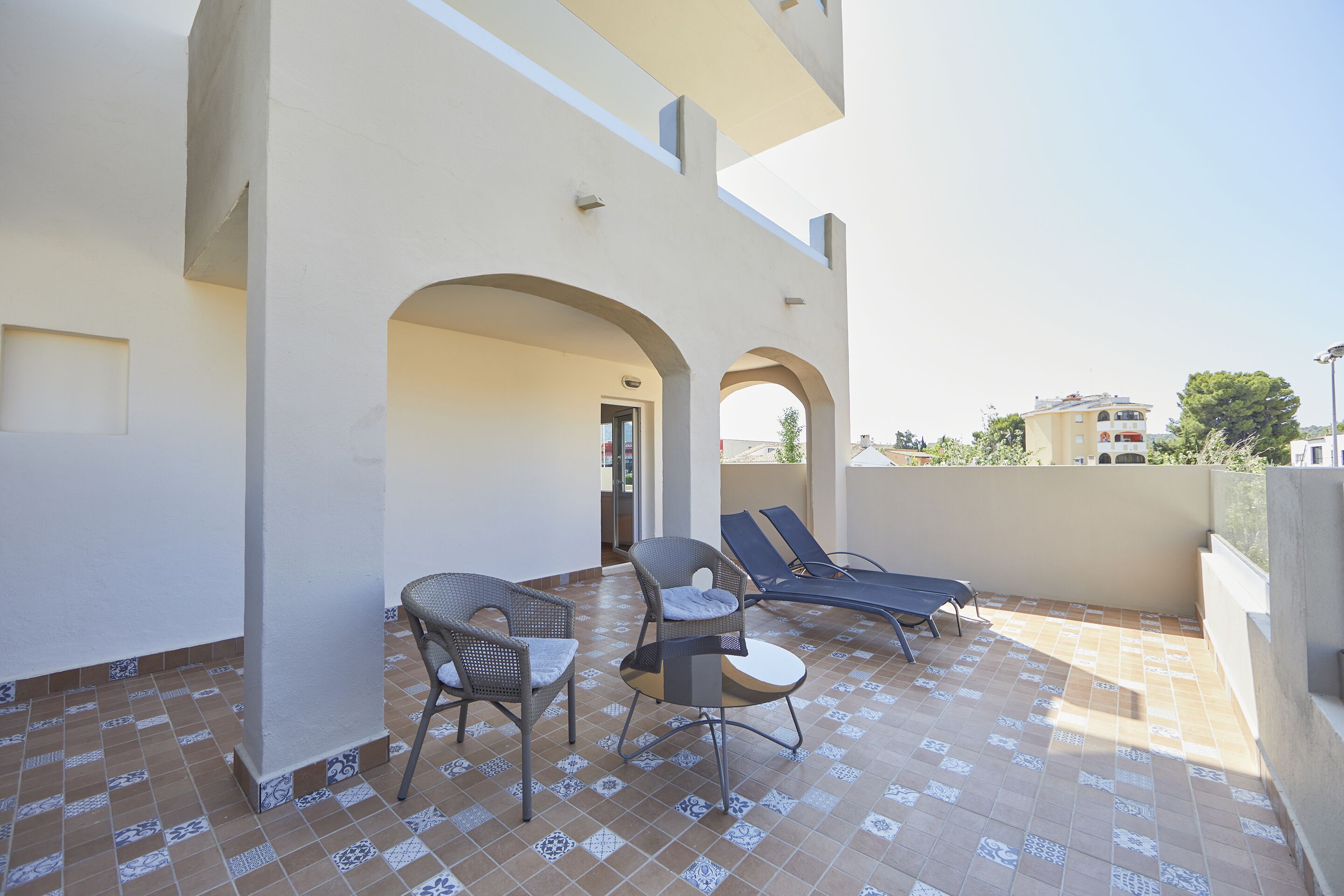 A rooftop terrace with a tiled floor, two wicker chairs, a small round table, and two lounge chairs.