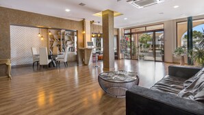 Un lobby amplio con piso de madera, un área de descanso con un sofá y una mesa de centro redonda, y una estantería llena de libros.