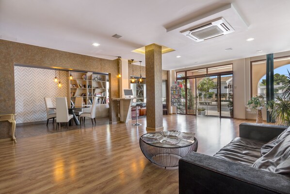 Un lobby amplio con piso de madera, un área de descanso con un sofá y una mesa de centro redonda, y una estantería llena de libros.