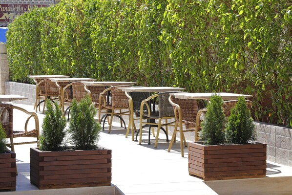 Outdoor seating with wicker chairs and tables, surrounded by neatly trimmed hedges and small potted plants. - Nura Santa Ponsa Pins (Calvia)