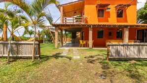 A two-story house with a balcony, surrounded by palm trees and a wooden fence. - PF12 - Ótima Casa 3 Quartos - Açu da Torre (Mata de São João)