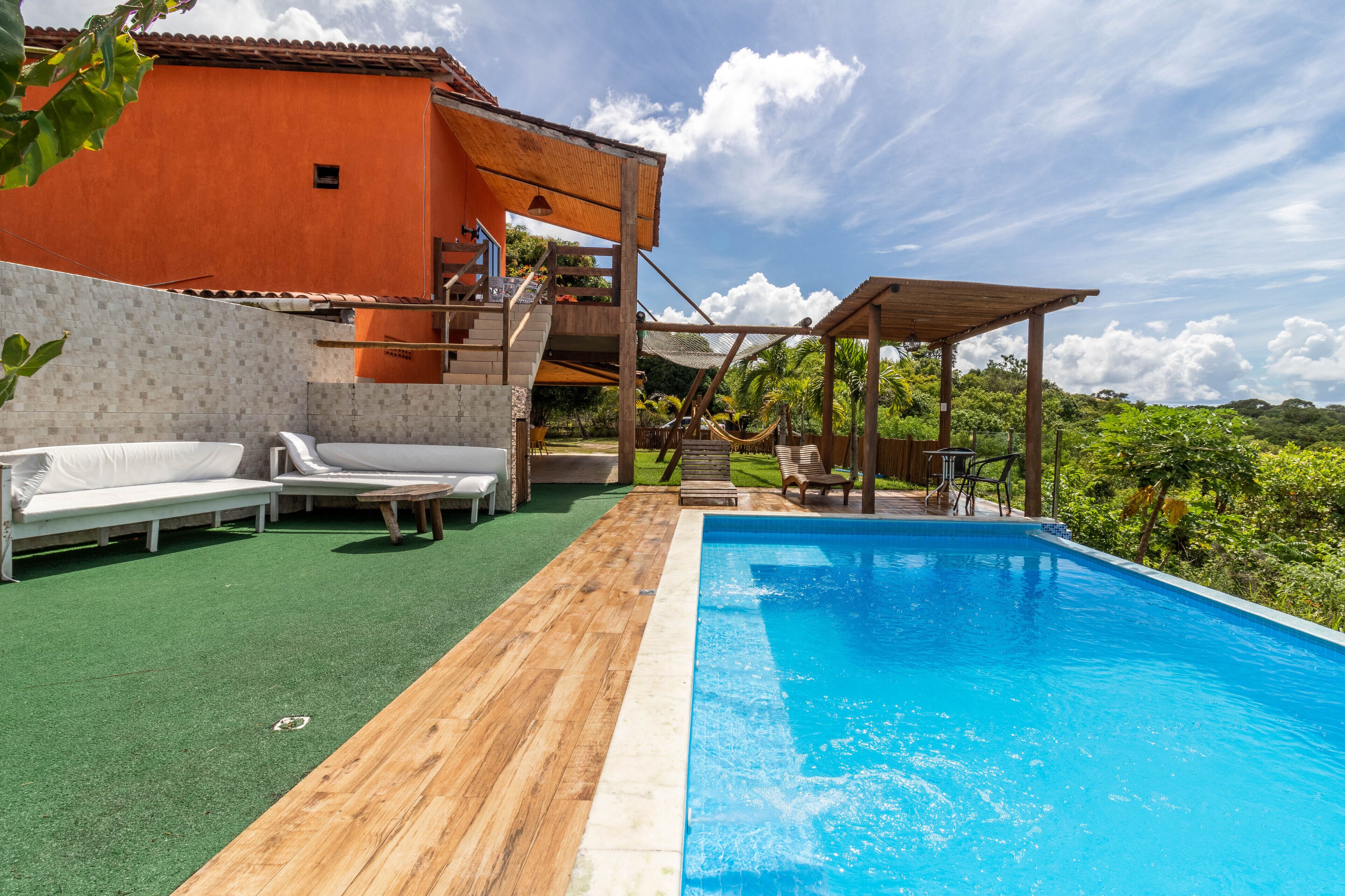 Ein Schwimmbecken mit Holzterrasse, weißen Liegestühlen und einer überdachten Sitzgelegenheit.