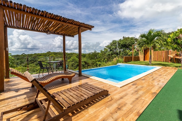 A wooden deck with a pool, lounge chairs, and a pergola.