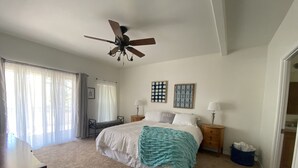 Ein Schlafzimmer mit einem Bett, zwei Nachttischlampen, einem Deckenventilator, einem Fenster mit Vorhängen und einem kleinen Tisch mit Stuhl.