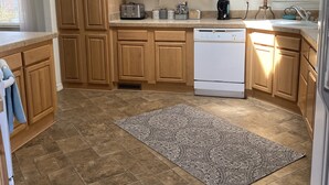 Eine Küche mit Holzausstattung, einem weißen Geschirrspüler, einem gemusterten Teppich und einer Uhr an der Wand.