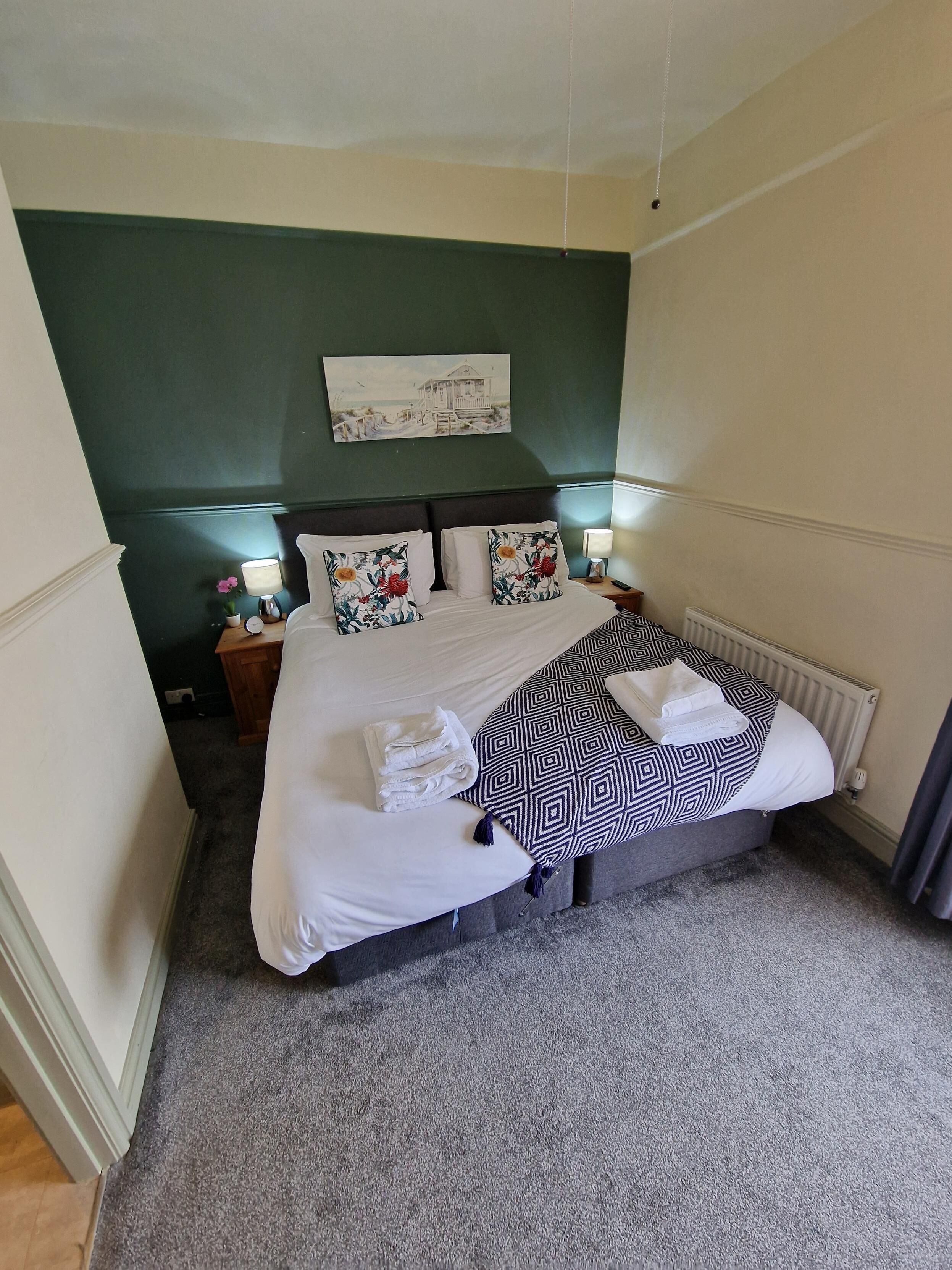 A neatly made bed with white linens and patterned pillows, a bedside lamp, and a framed picture on the wall.