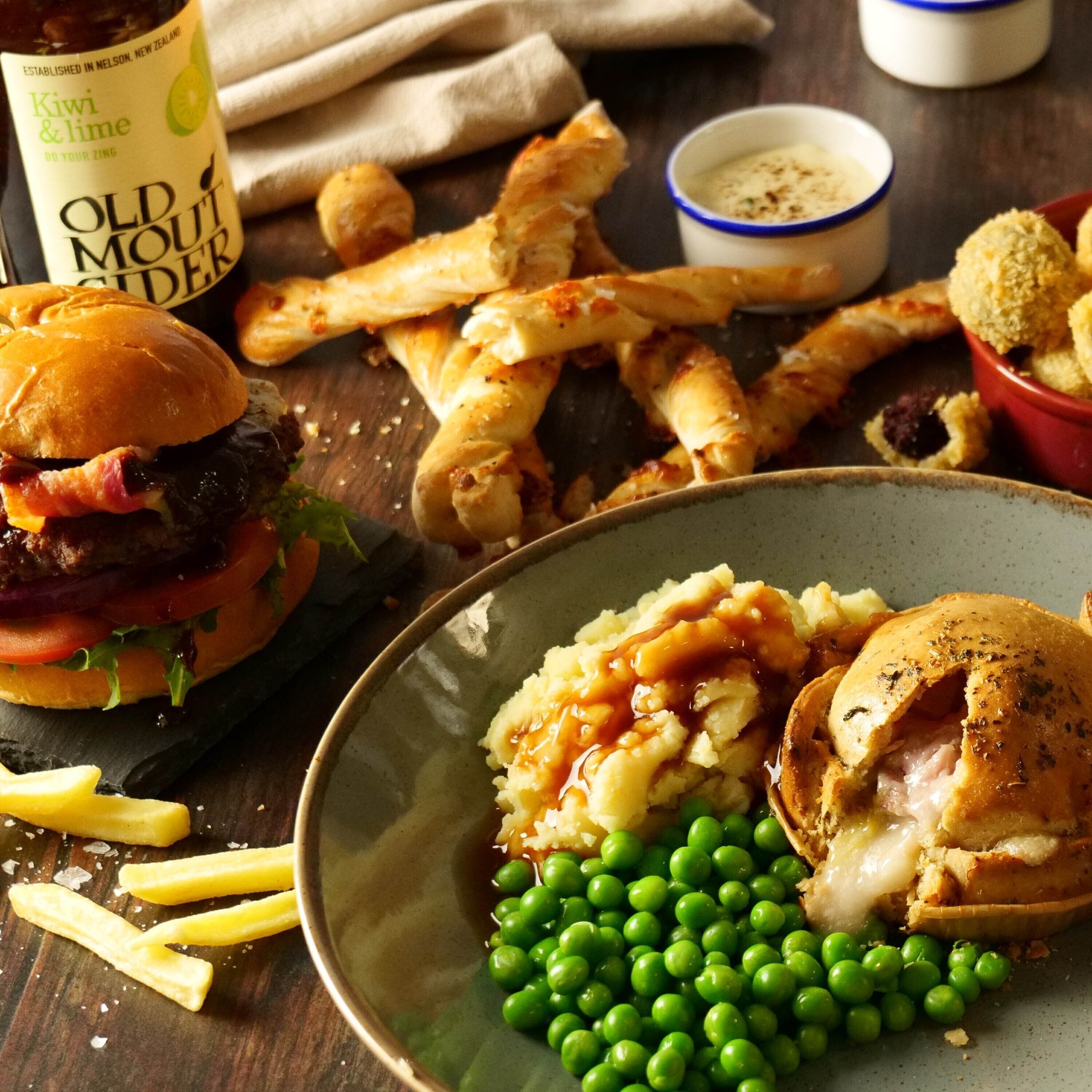 A meal with a burger, fries, peas, mashed potatoes, and a drink.