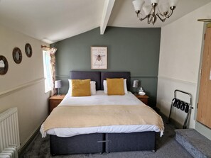 A bedroom with a bed, two nightstands, a wall-mounted lamp, a radiator, and a ceiling light fixture. - The Foresters Arms (Tarporley)