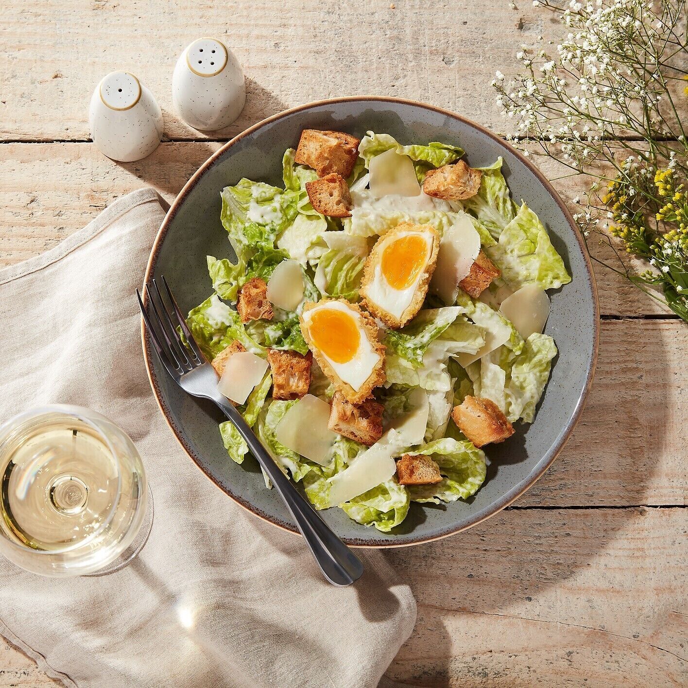 A bowl of salad with croutons and a hard-boiled egg on a wooden table.