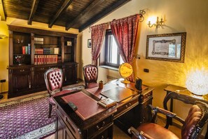 Quarto com escrivaninha de madeira, duas poltronas de couro, um globo e uma estante repleta de livros.