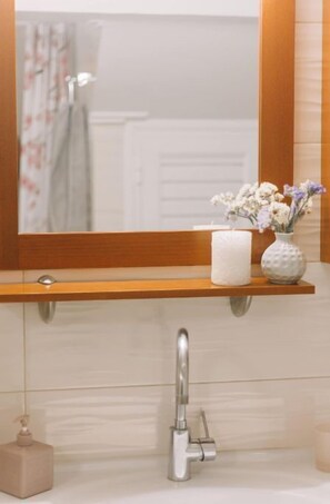 A bathroom with a mirror, a shelf with a candle and flowers, a faucet, and a soap dispenser. - Debbie's House (Kalamata)