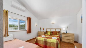 Une chambre à coucher comprenant un lit, une table de chevet, une fenêtre avec des rideaux et un appareil de climatisation.