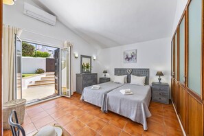 A bedroom with two beds, a sliding glass door leading to a patio, a bedside table with a lamp, and a wall-mounted mirror.