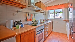 Une cuisine avec des meubles en bois, un four encastré, une machine à café et une fenêtre donnant sur l’extérieur.
