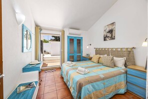 A bedroom with a bed, a bedside table, a mirror, a wardrobe, and a door leading to an outdoor area.