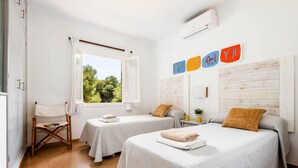 Una habitación con dos camas, una ventana que da a árboles y una pared con decoraciones coloridas.