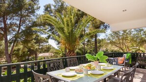 Un área de comedor al aire libre con una mesa preparada para dos personas, rodeada de sillas, con vista a árboles y una cerca.