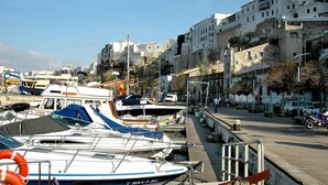 Una marina con barcos amarrados, una calle con edificios y un cielo despejado.