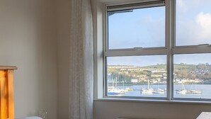 Une chambre d’hôtel avec un lit, une fenêtre donnant sur un port et une tête de lit en bois.