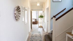 Un couloir doté d’un plancher en bois, d’un tapis bleu et blanc, d’une plante et d’un escalier avec une rampe en bois.
