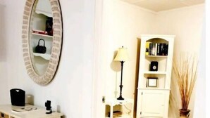 A room with a wooden floor, a white cabinet with books, a lamp, and a mirror on the wall.