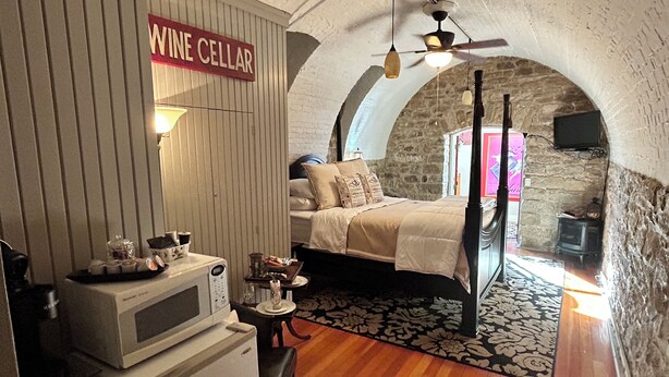 A cozy room with a bed, a small table, a microwave, and a sign reading "WINE CELLAR". - Unique wine cellar suite in the heart of Downtown Hermann! (Hermann)