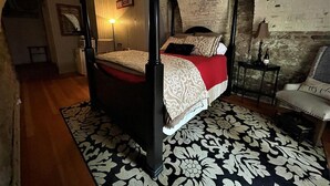 A four-poster bed with a red and white bedspread, a black and white patterned rug, and a small table with a lamp. - Unique wine cellar suite in the heart of Downtown Hermann! (Hermann)