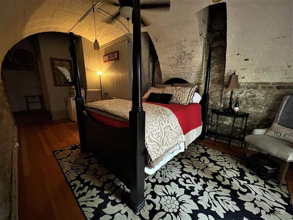 A four-poster bed with a red and white bedspread, a black and white patterned rug, and a small table with a lamp.