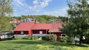 A red barn with a white picket fence, surrounded by greenery and other buildings in the background. - Unique wine cellar suite in the heart of Downtown Hermann! (Hermann)