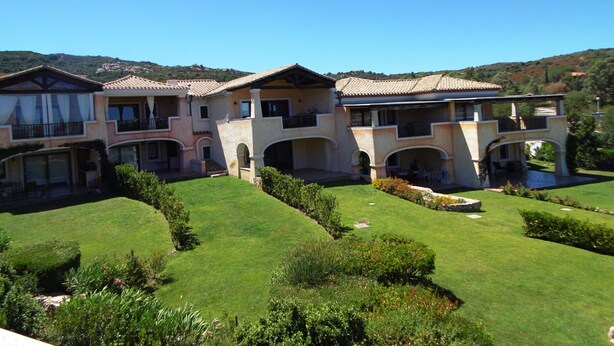 Una casa grande de varios pisos con un patio interior, con varios balcones y un césped bien cuidado.