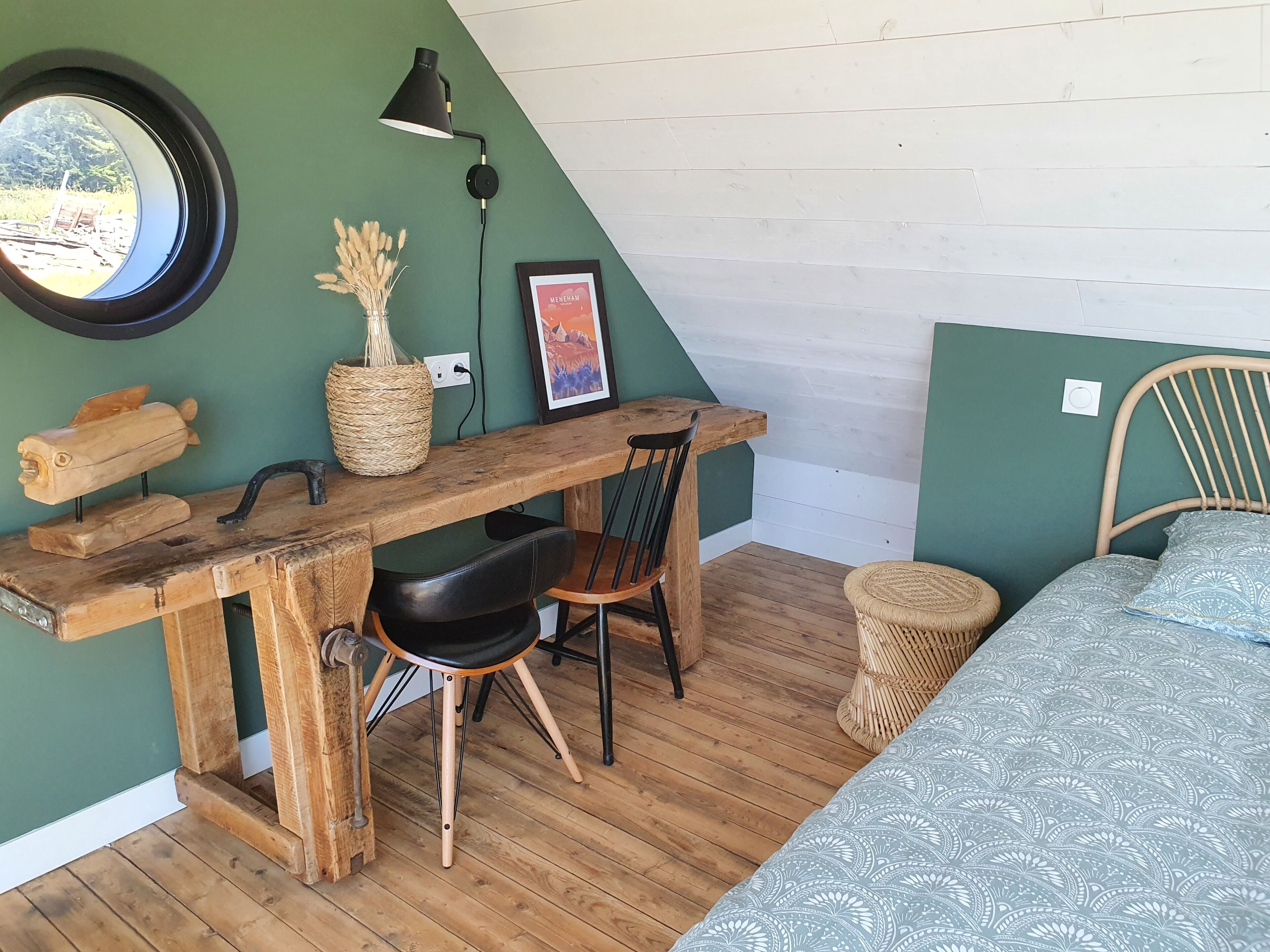 Ein gemütliches Zimmer mit Schreibtisch aus Holz, einem Sessel, einem Bett und einem runden Spiegel an der Wand.