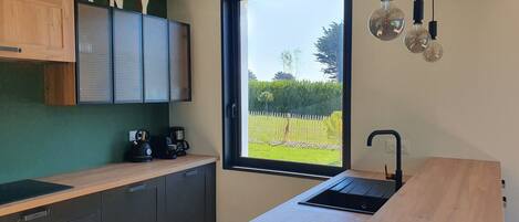 A modern kitchen with a wooden countertop, dark cabinets, a built-in stove, and a window with a view of a garden.