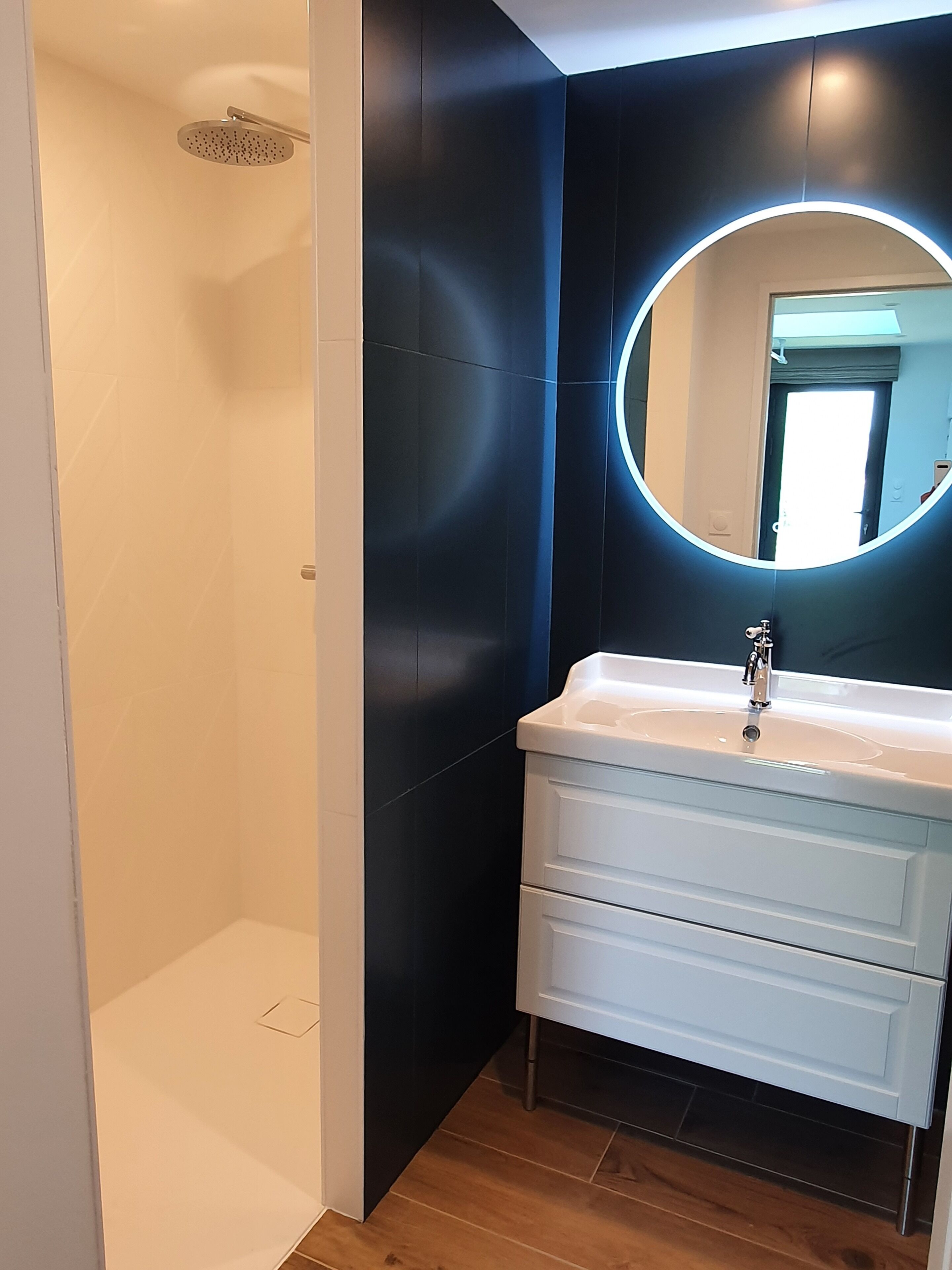 A bathroom with a white sink, a round mirror, and a shower.