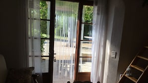 Une pièce avec une chaise en bois, une petite table et un canapé avec un coussin. On y trouve une échelle en bois et une lanterne blanche sur le côté droit.