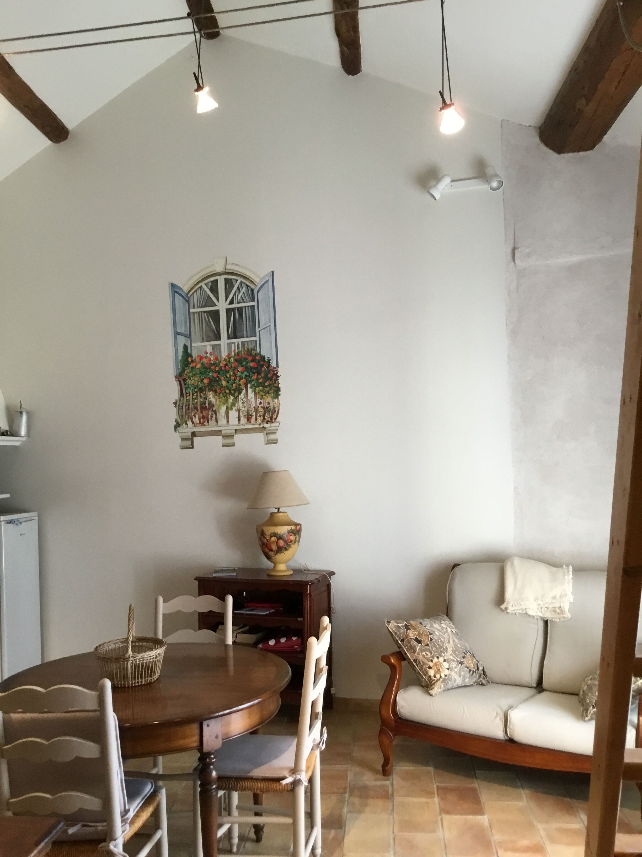 Un coin repas comprenant une table ronde en bois, des chaises, un canapé, une lampe et une fenêtre fixée au mur, offrant une vue sur la verdure.