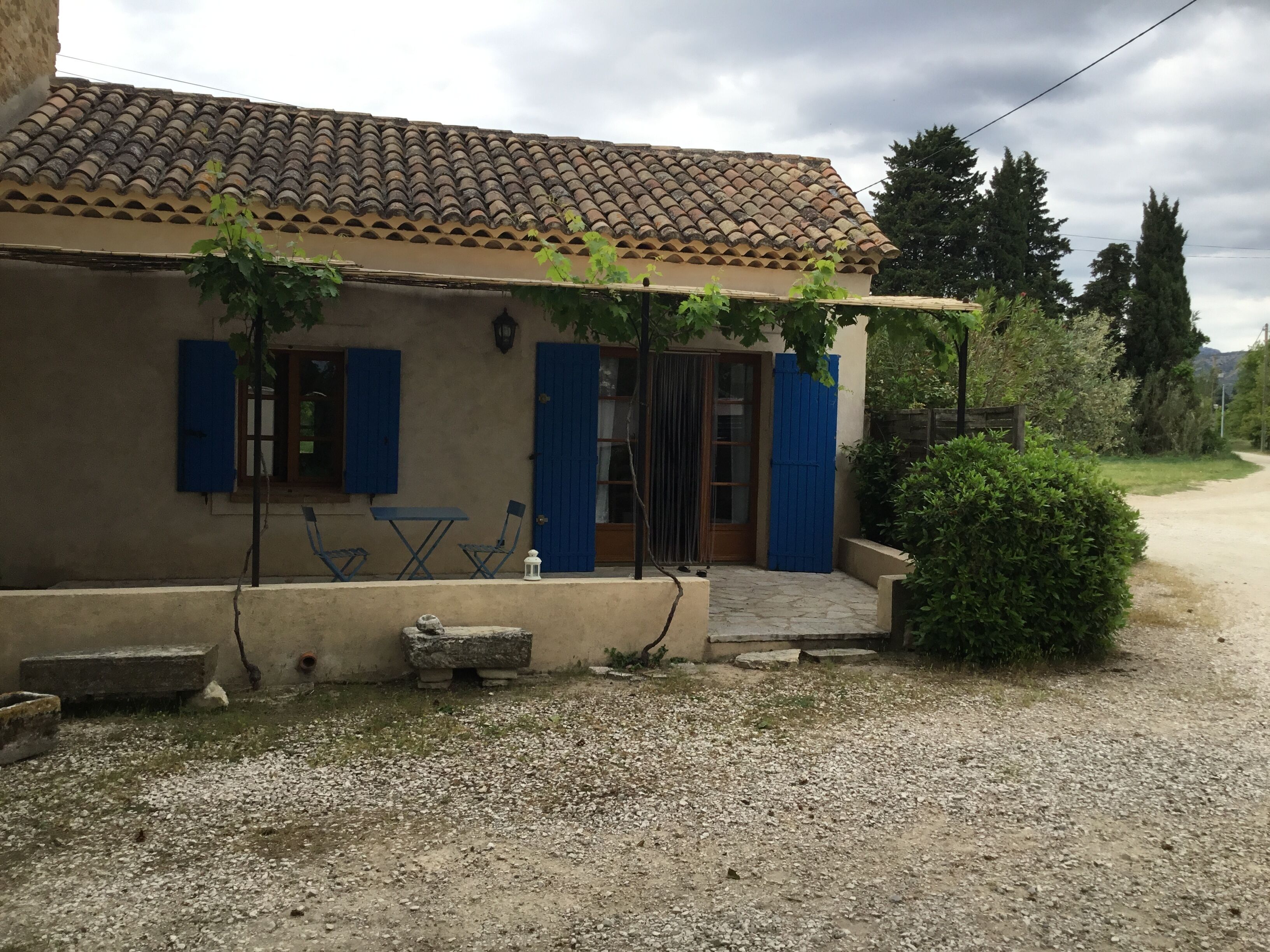 Une maison de campagne au toit recouvert de tuiles, aux volets bleus et à l’allée gravillonnée.