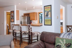 A modern kitchen with wooden cabinets, a stainless steel refrigerator, and a dining area with a table and chairs.