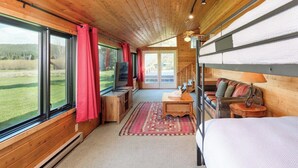 Een knus houten interieur met grote ramen, een bed, een bank en een kleine tafel.