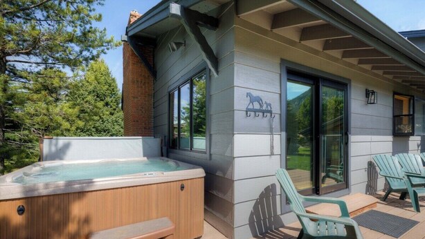 Een bubbelbad met houten banken, een overdekt terras met Adirondack-stoelen en een gebouw met een paardenlogo.