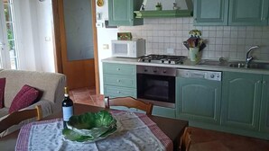 Une cuisine chaleureuse avec des meubles de couleur verte, un poêle et une table à manger dressée pour deux personnes.