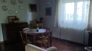 Un coin repas avec une table ronde, des chaises et un canapé. Il y a une fenêtre avec des rideaux et un climatiseur fixé au mur.