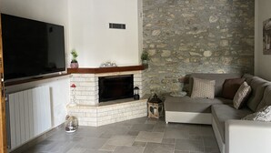 Un salon avec un mur en pierre, une cheminée, un téléviseur à écran plat et un canapé.