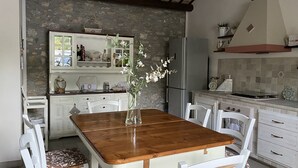 Une cuisine avec un mur en pierre, un plafond en bois, des armoires blanches et une table à manger en bois avec des chaises.