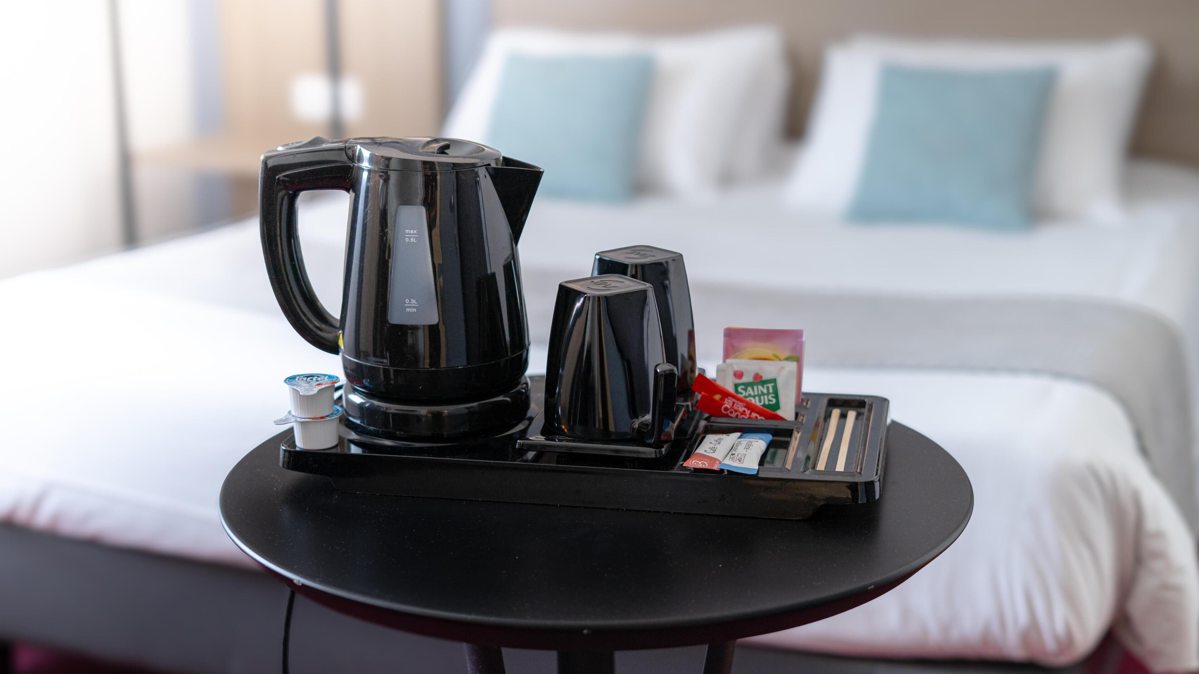 A hotel room with a bed, pillows, a coffee maker, a tray with a coffee pot, a milk carton, and a packet of sugar.