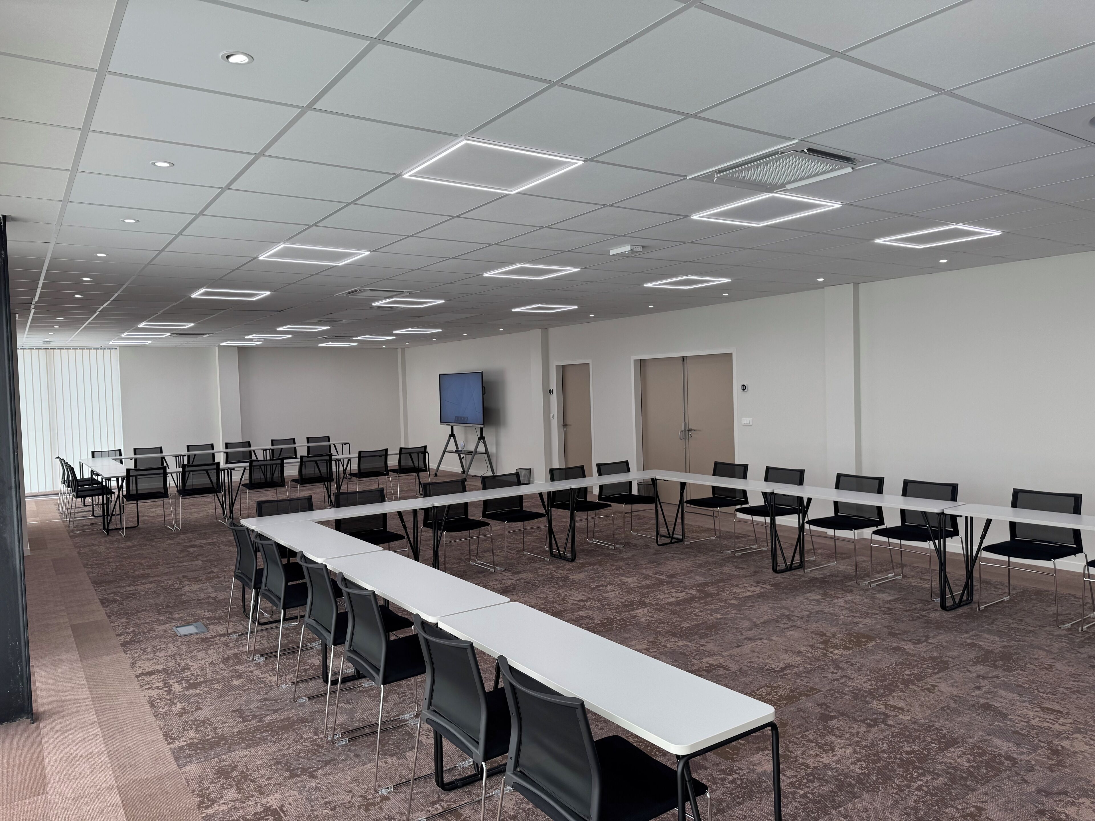 A conference room with a long table, chairs, a projector screen, and a carpeted floor.