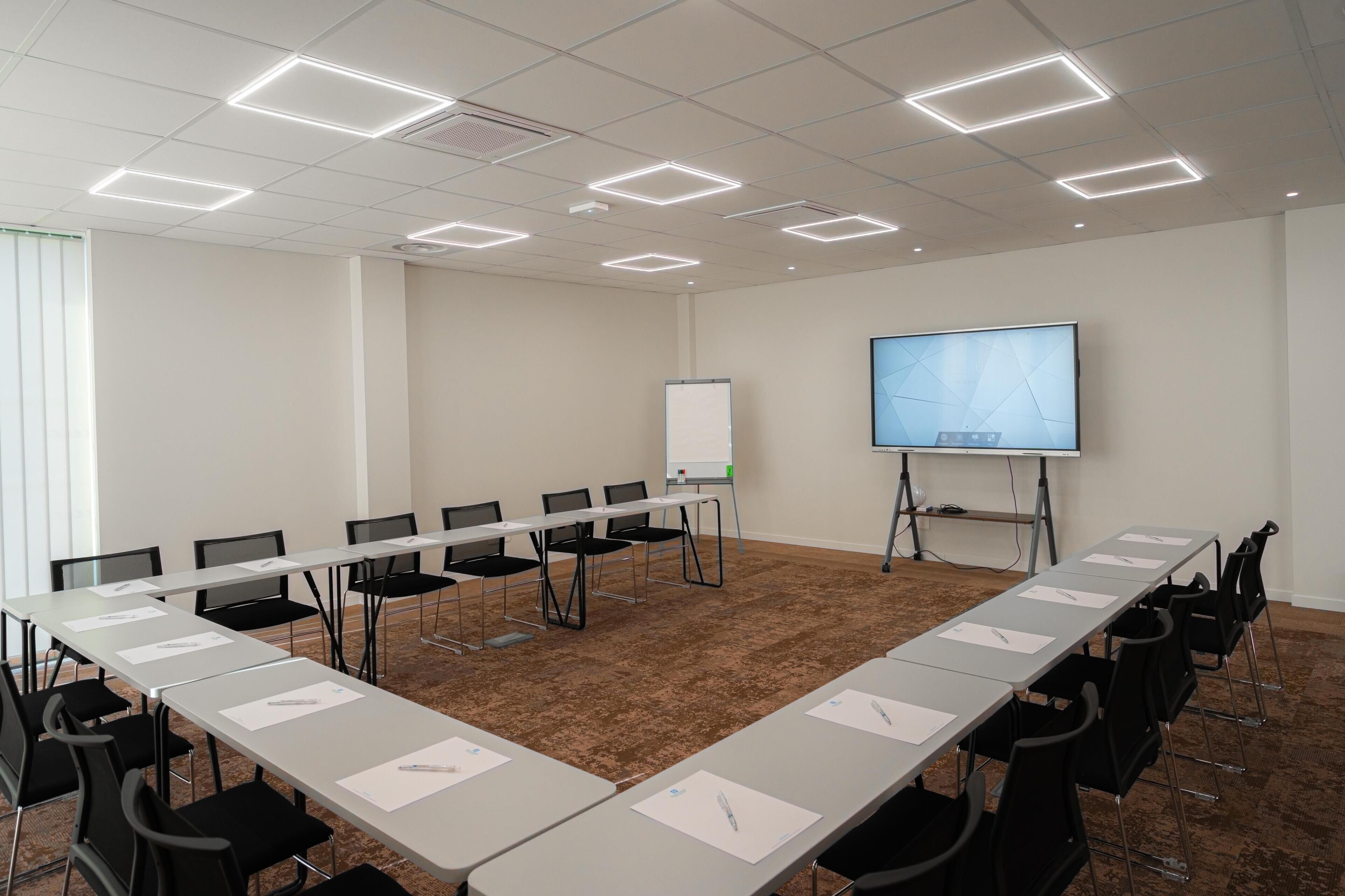 Una sala de conferencias con una larga mesa, sillas, una pizarra y una pantalla para proyector.