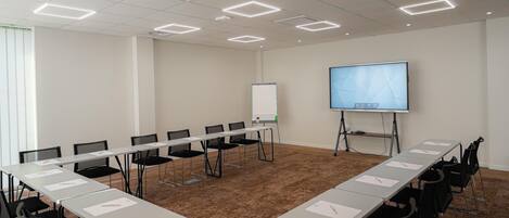 Una sala de conferencias con una larga mesa, sillas, una pizarra y una pantalla para proyector.