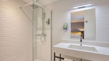 Un baño moderno con cabina de ducha de vidrio, un lavabo blanco y un espejo grande.
